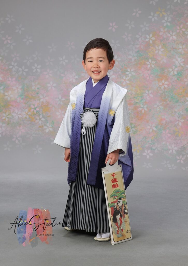 羽織袴姿の男の子の単独ショット。千歳飴を手に持ち、誇らしげな表情を見せてくれています。グラデーションの美しい紫色の羽織と、ストライプ柄の袴が凛々しさを引き立てています。